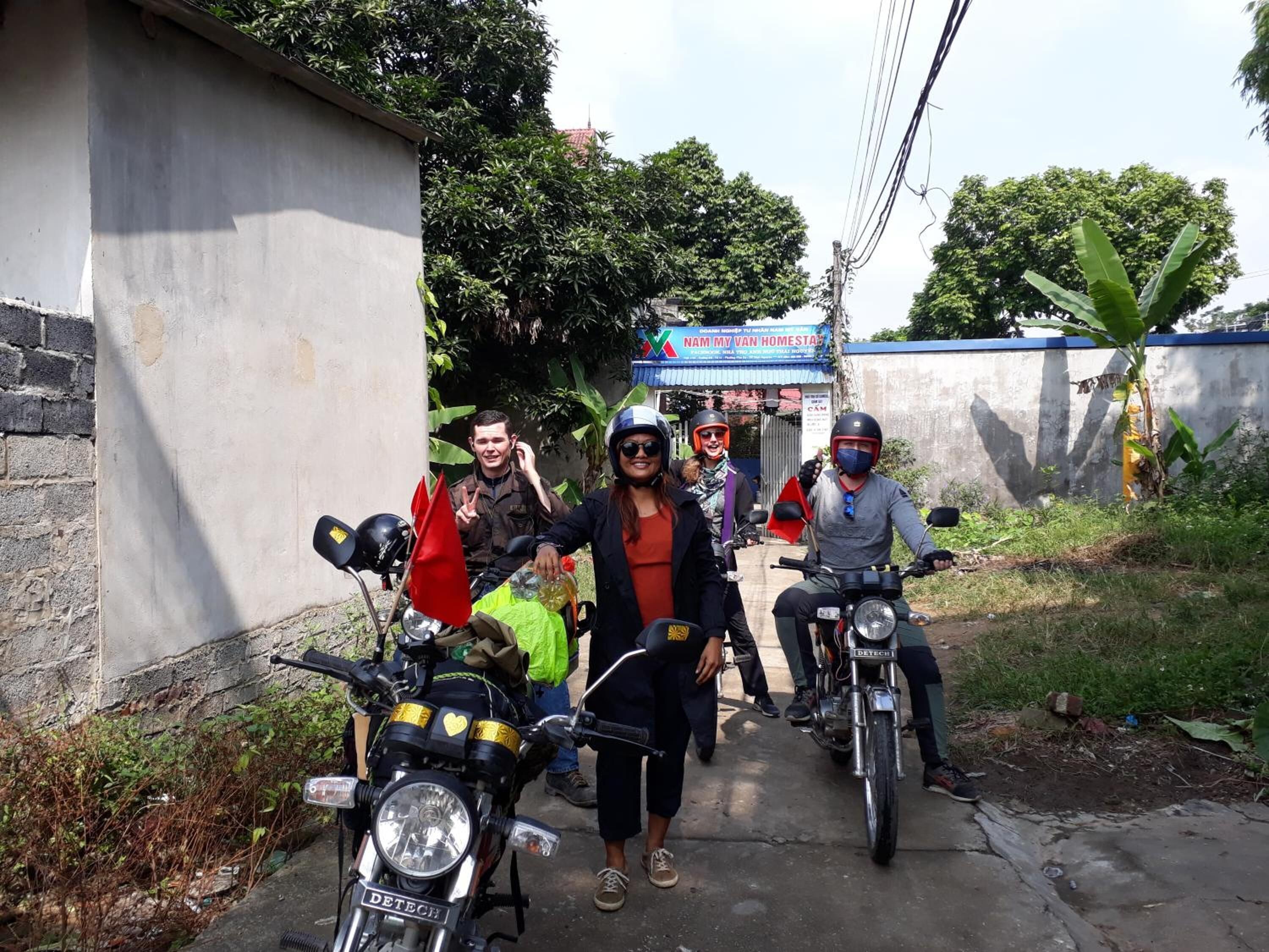A group of people on motorcycles parked on a narrow street with a building in the background.