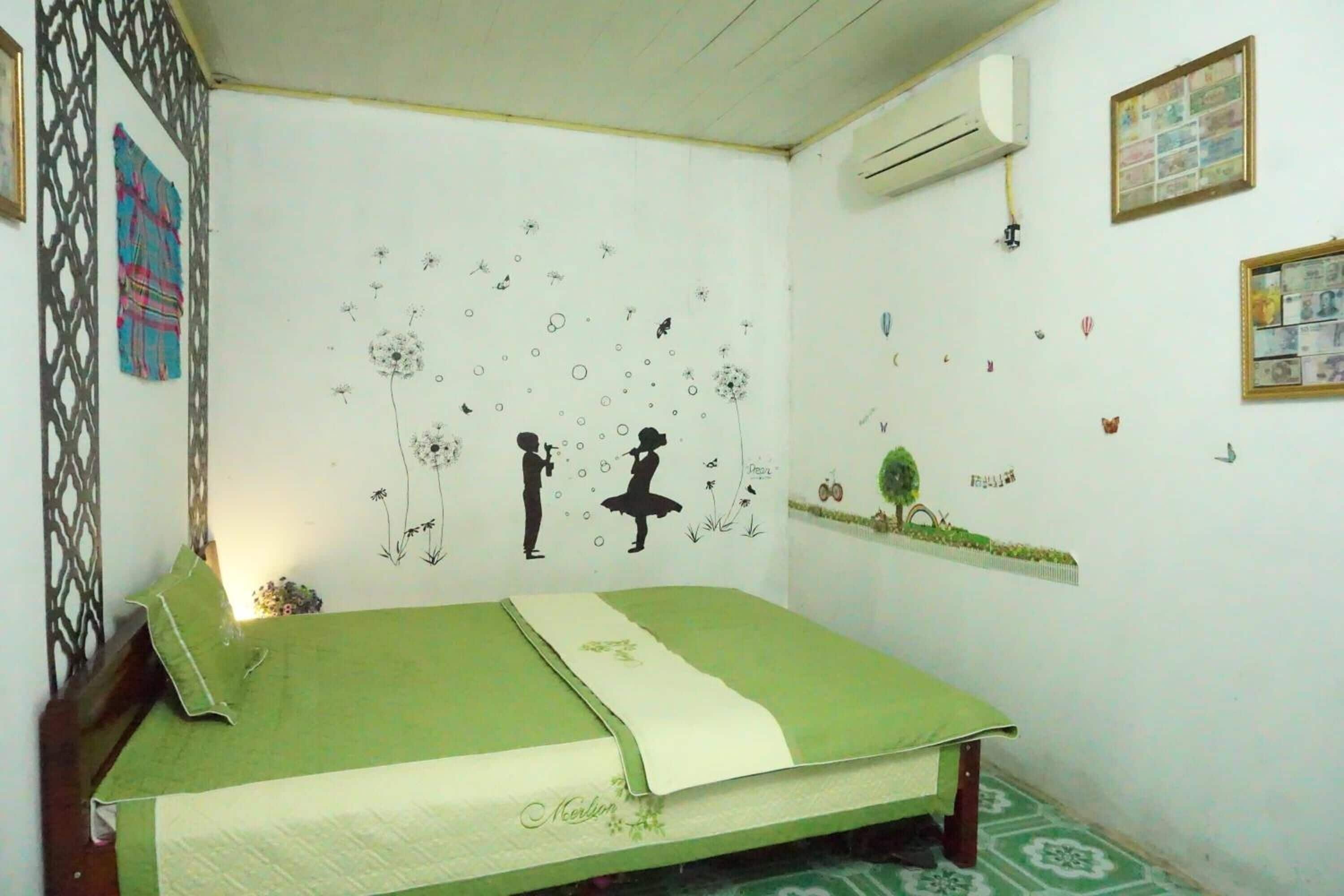 Un dormitorio con una colcha verde, una pared decorada con varios adhesivos y un equipo de aire acondicionado montado en la pared.