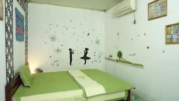 Un dormitorio con una colcha verde, una pared decorada con varios adhesivos y un equipo de aire acondicionado montado en la pared.