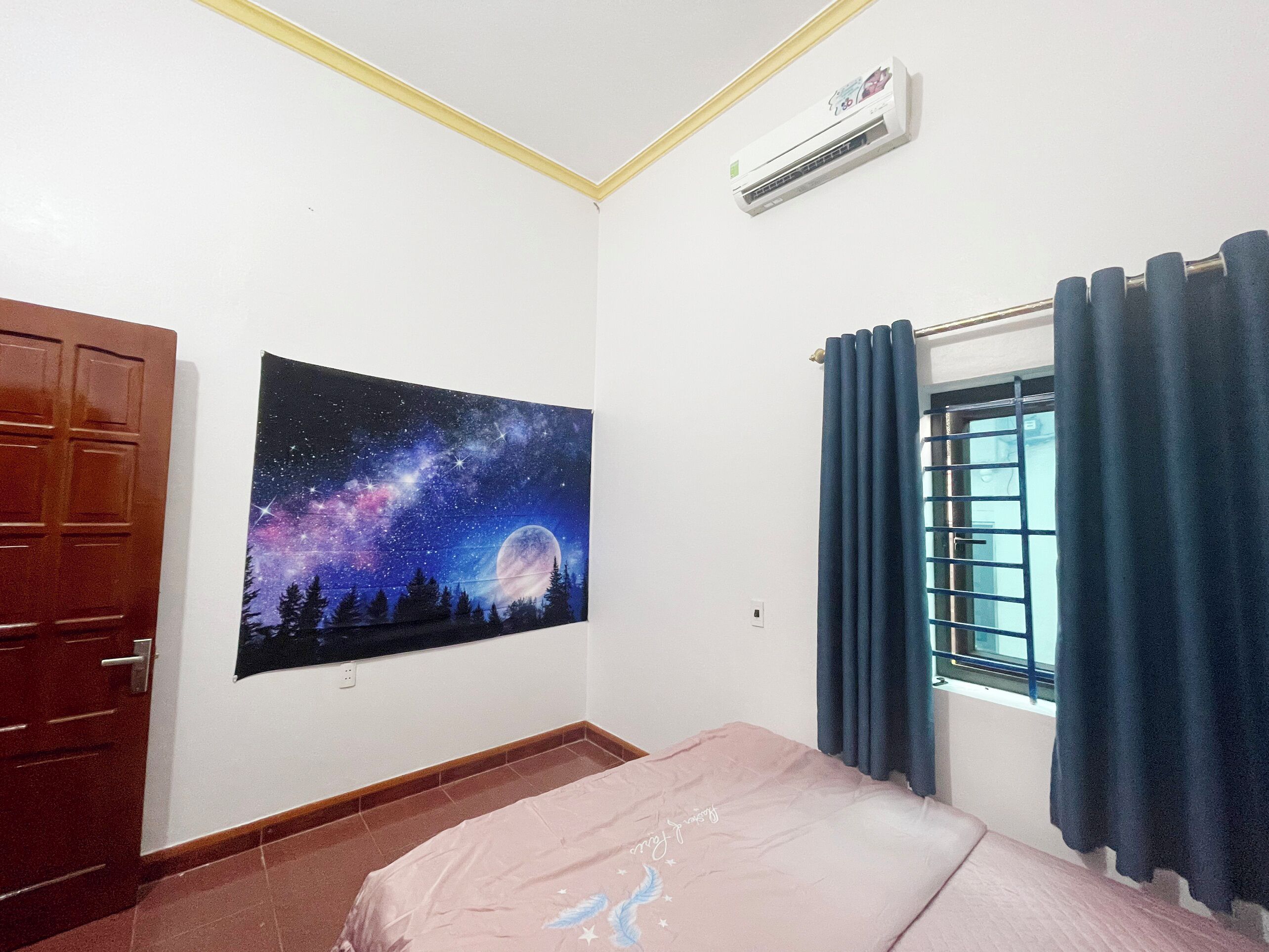 Ein Schlafzimmer mit einem Bett, einem Wandgemälde des Nachthimmels, einem Fenster mit Vorhängen und einer Klimaanlage.