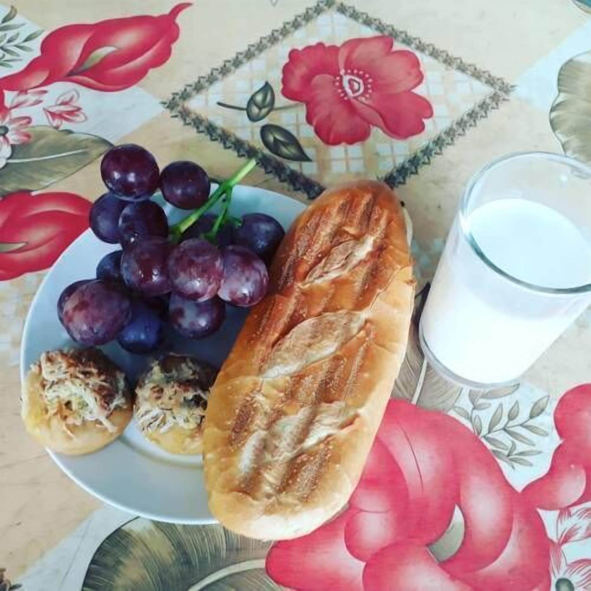 A plate with grapes, a baguette, and a glass of milk on a table with a floral tablecloth.