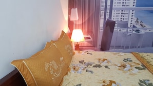 Hotellihuone, jossa on sänky, yöpöytä, lamppu ja näkymä kaupunkimaisemaan.