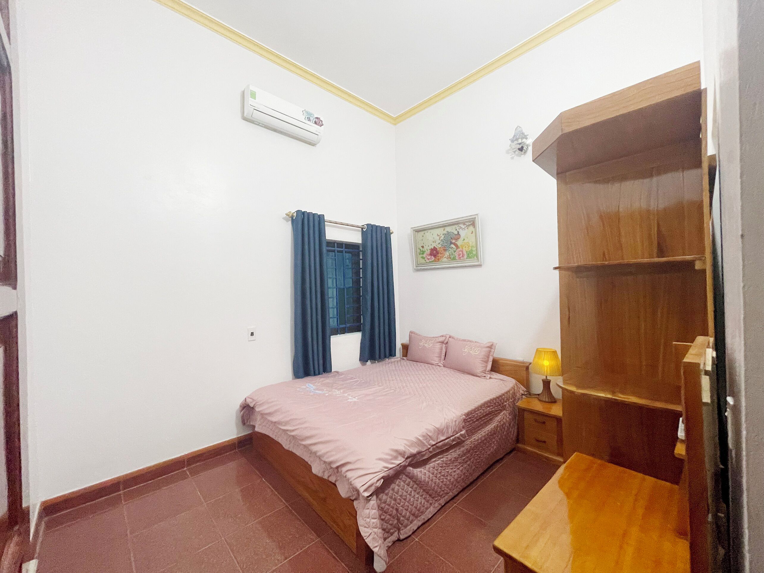 Quarto com cama, mesa de cabeceira, guarda-roupa, ar-condicionado, janela com cortinas e um quadro na parede.