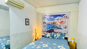 A bedroom with a bed, a nightstand, a lamp, and a wall-mounted air conditioner.