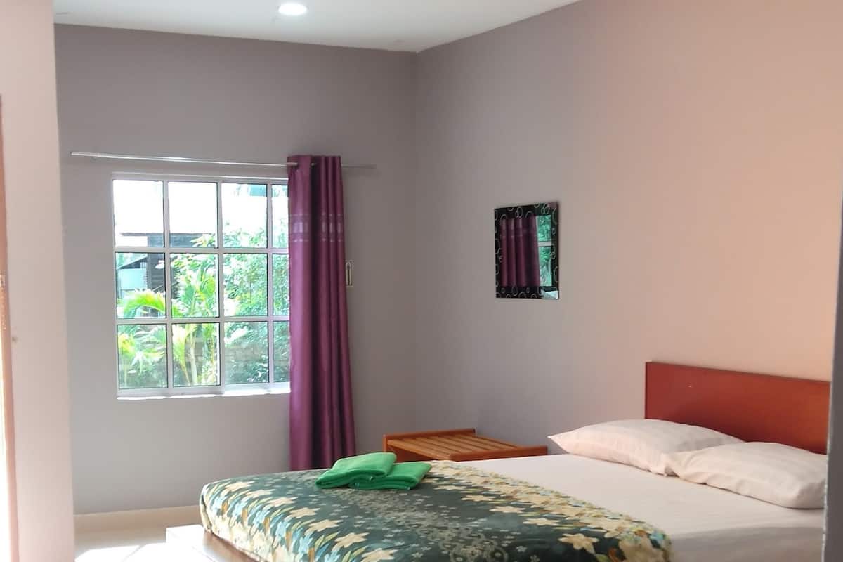 A bedroom with two beds, a window with curtains, and a view of greenery outside.