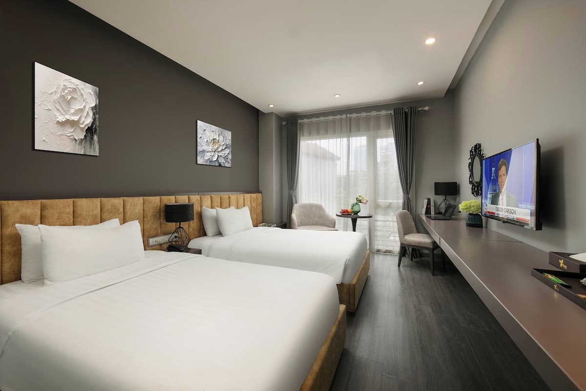Habitación de hotel con dos camas, televisión, escritorio y obras de arte en las paredes.