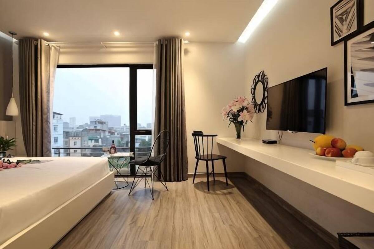 Una habitación de hotel moderna con una cama grande, un escritorio, una silla, un televisor y vistas a la ciudad.