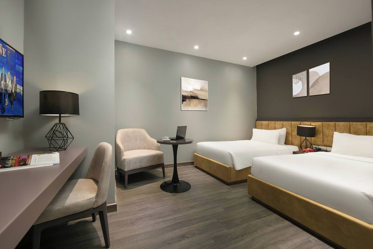 Habitación de hotel con dos camas, un escritorio con silla, una mesita y un televisor.