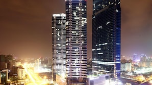 Deux immeubles de grande hauteur, dont les fenêtres sont illuminées la nuit, se dressent au milieu d’un paysage urbain.