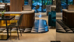 Un hall d’hôtel moderne doté d’un comptoir d’accueil, d’un espace salon et de grandes fenêtres offrant une vue sur l’extérieur.