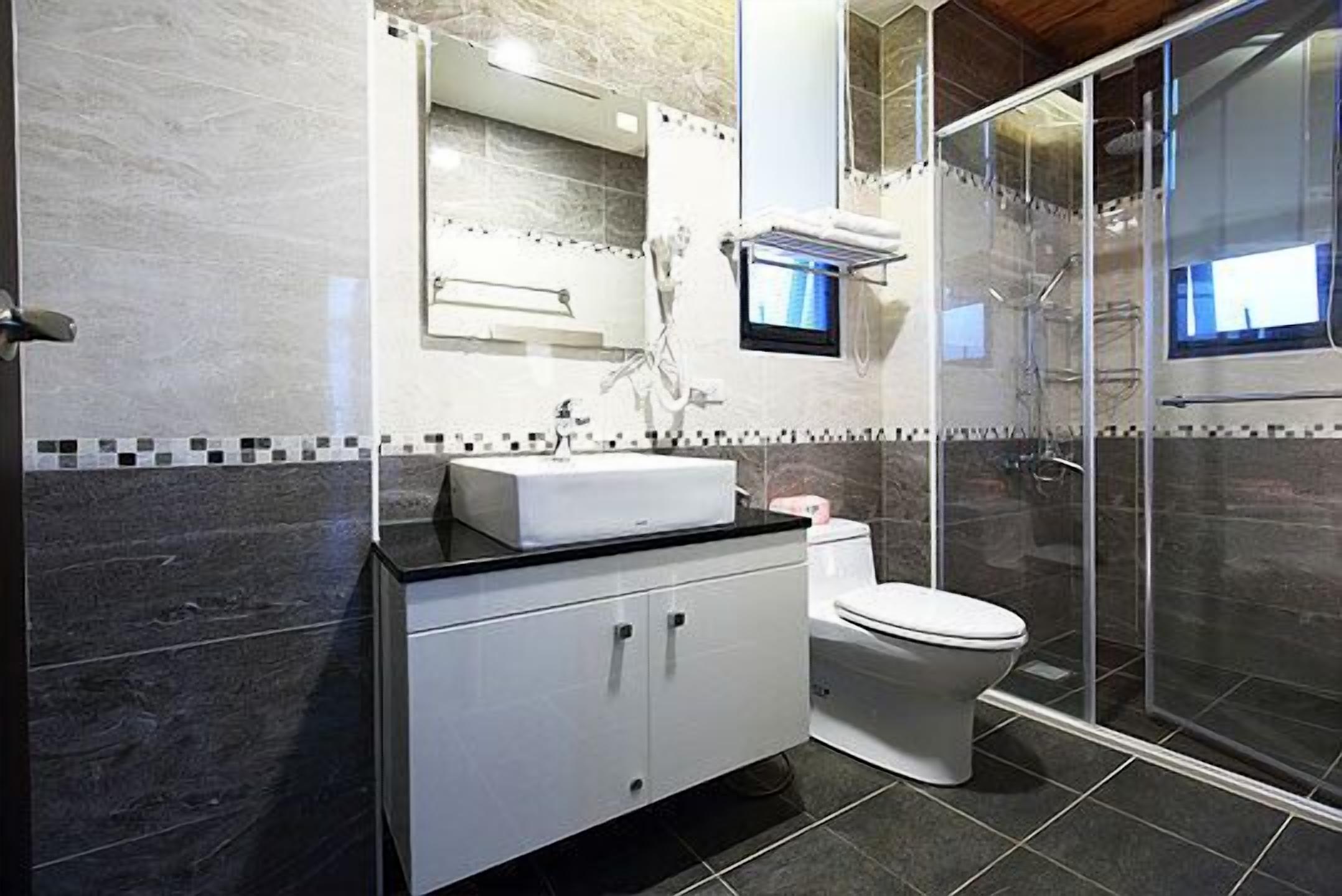 A modern bathroom with a white sink, toilet, and shower area.