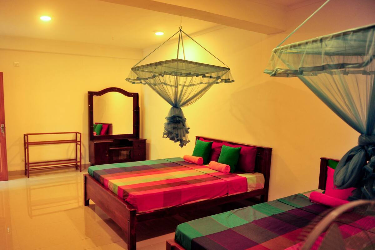 A bedroom with two beds, a wooden nightstand, a mirror, and a hanging mosquito net.