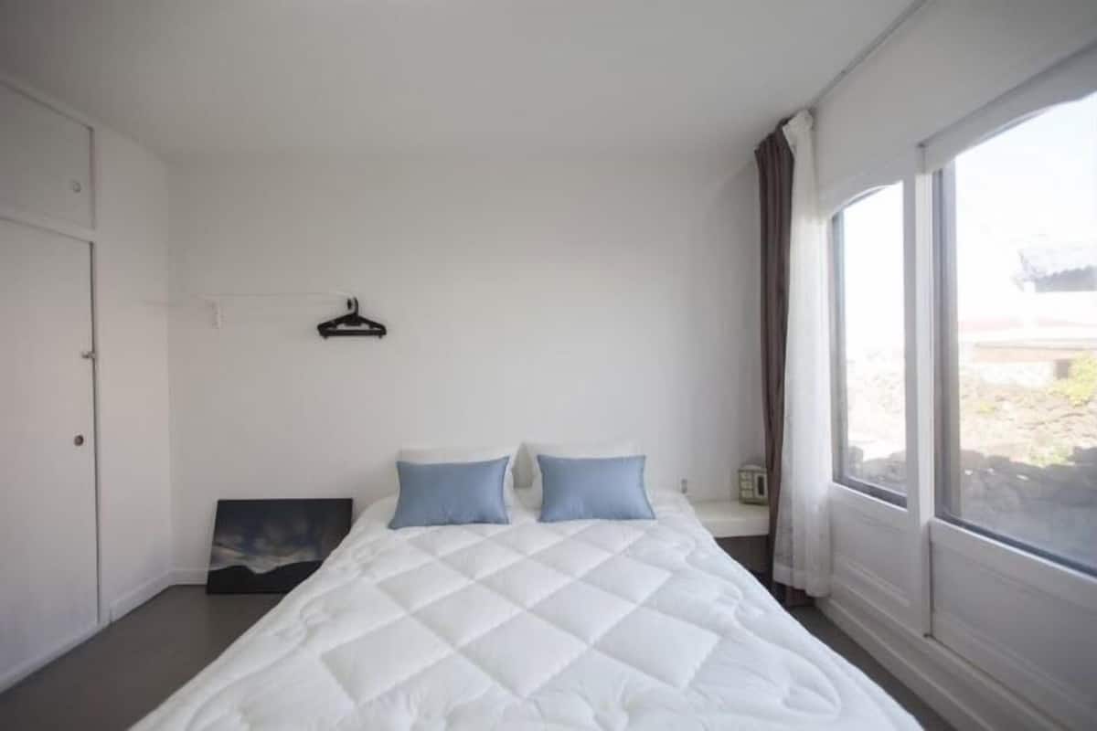 A bedroom with a bed, a painting on the wall, and a window with curtains.