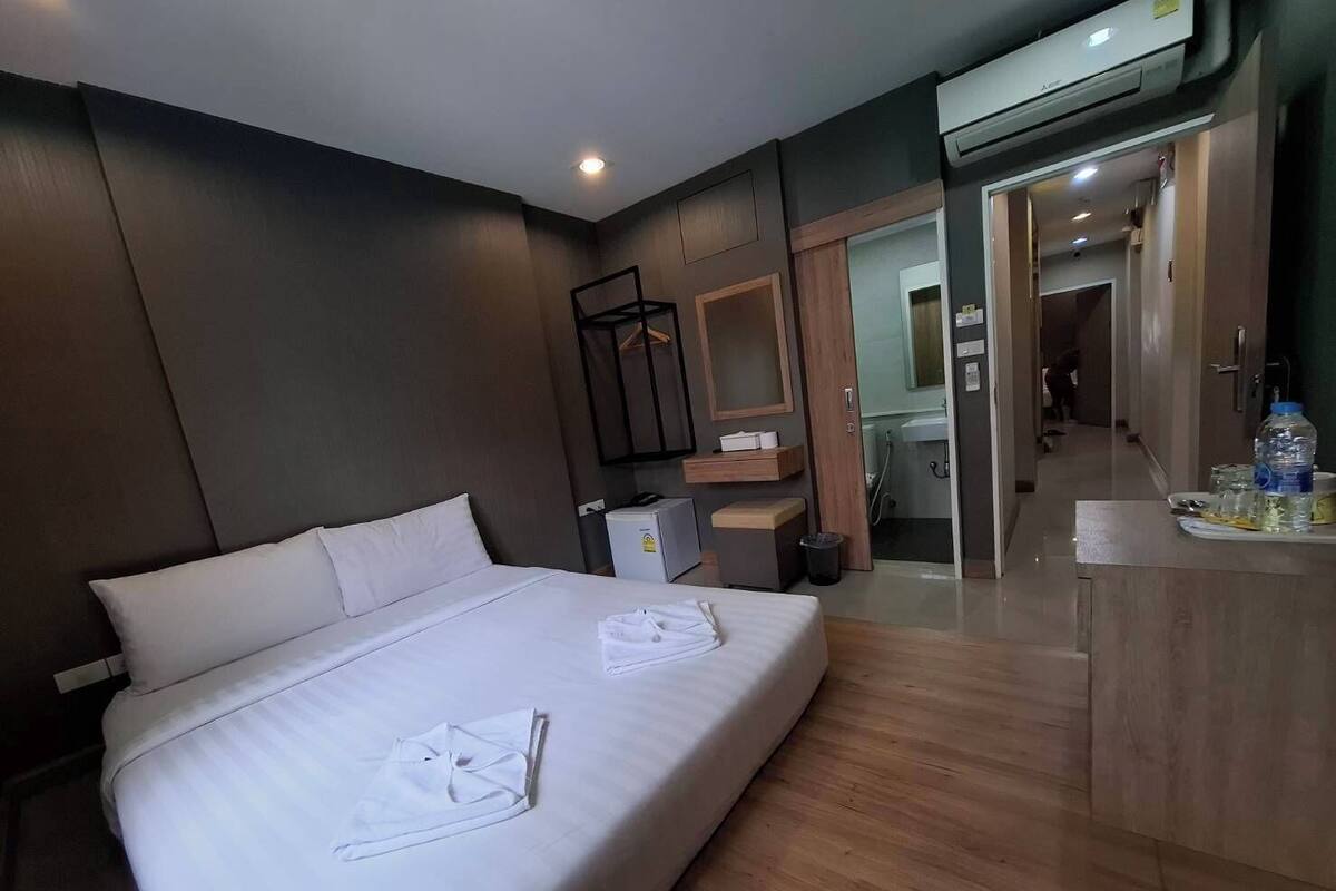 A modern hotel room with a large bed, a desk, and a bathroom visible through an open door.
