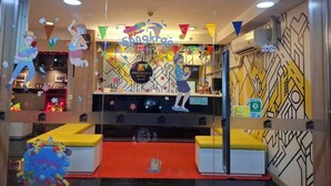A hotel reception area with a colorful interior, a central counter, and a seating area with a small table. - Collection O Pratunam 19 Hotel (Bangkok)
