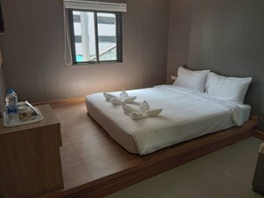 Een net opgemaakt bed met witte lakens en handdoeken, een nachtkastje met een waterfles en een beker, en een raam met jaloezieën.