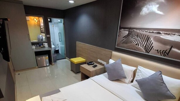 A hotel room with a large bed, a bedside table with a lamp, a wall-mounted TV, and a view of the beach. - Collection O Pratunam 19 Hotel (Bangkok)