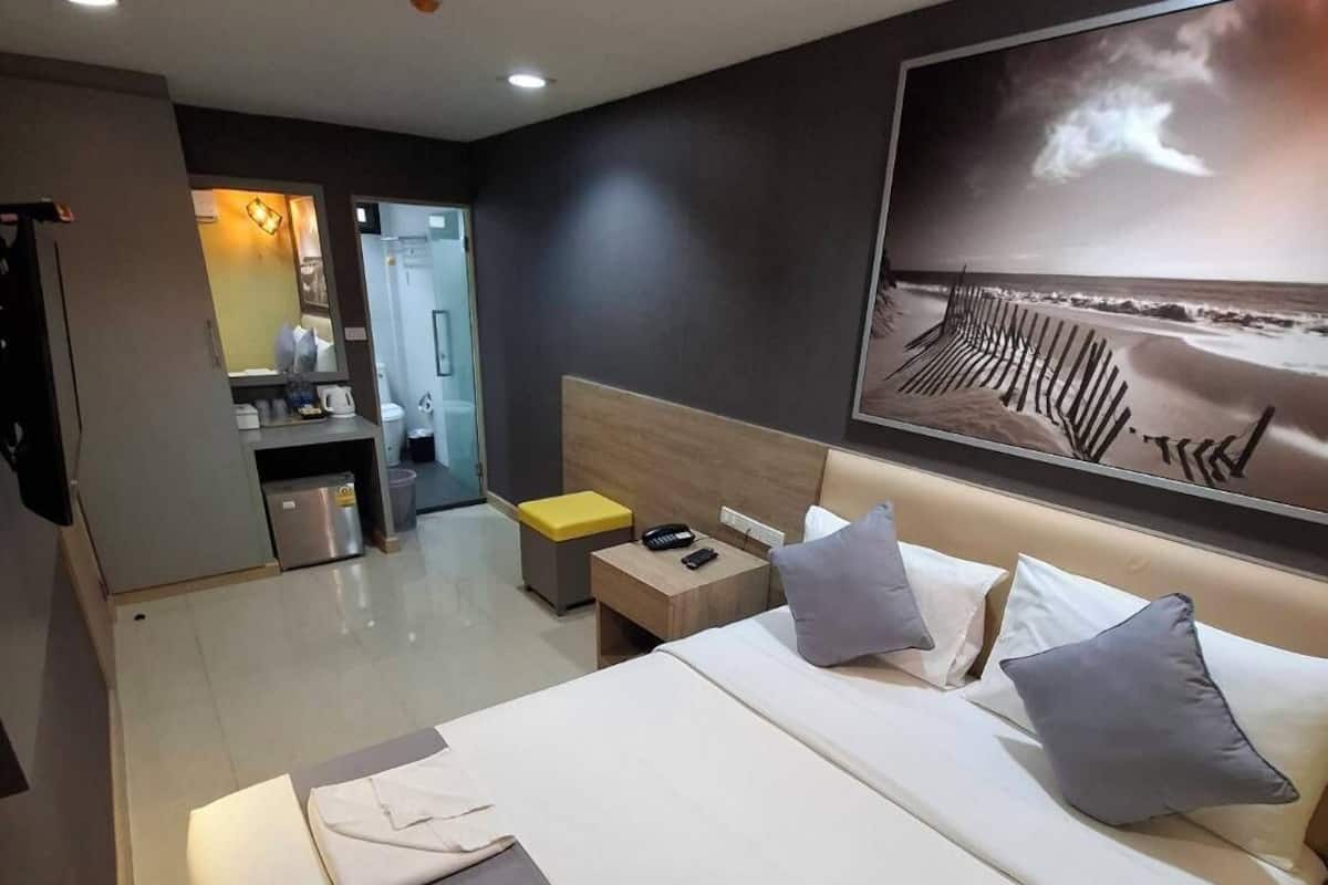 A hotel room with a large bed, a bedside table with a lamp, a wall-mounted TV, and a view of the beach.