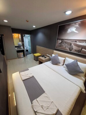 Habitación de hotel con una cama grande, una mesita de noche con lámpara, televisor montado en la pared y vistas a la playa.