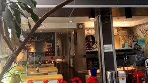 A modern hotel entrance with a glass facade, potted plants, and a sign indicating the name and location. - Collection O Pratunam 19 Hotel (Bangkok)