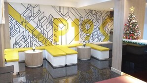 A modern lobby with geometric patterned walls, yellow and white seating, a Christmas tree, and a reflective floor. - Collection O Pratunam 19 Hotel (Bangkok)