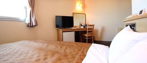 A hotel room with a bed, a desk with a computer, a chair, and a bedside table.