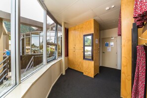 A hotel corridor with a wooden wall, a window with a view of a building and greenery, and a door with a sign. - Tahuna Pod Hostel (Queenstown)