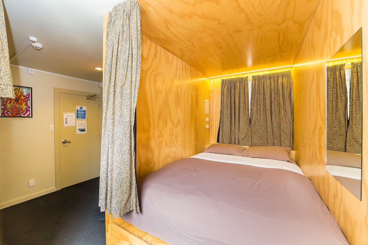 Ein hölzernes Himmelbett mit Spiegel an der Kopfteil, gemusterten Vorhängen und einer Tür mit einem Schild.