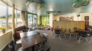 A modern interior with a large table and chairs, a sofa, and a view of the outdoors through large windows. - Tahuna Pod Hostel (Queenstown)