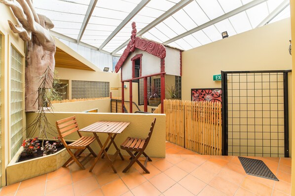 A room with a wooden table and chairs, a large decorative sculpture, and a small house-like structure with red trim.