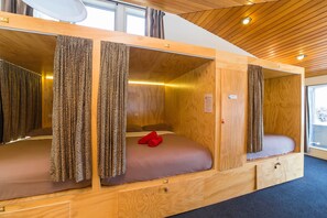 A cabin with three wooden beds, each with a curtain and a small drawer. - Tahuna Pod Hostel (Queenstown)