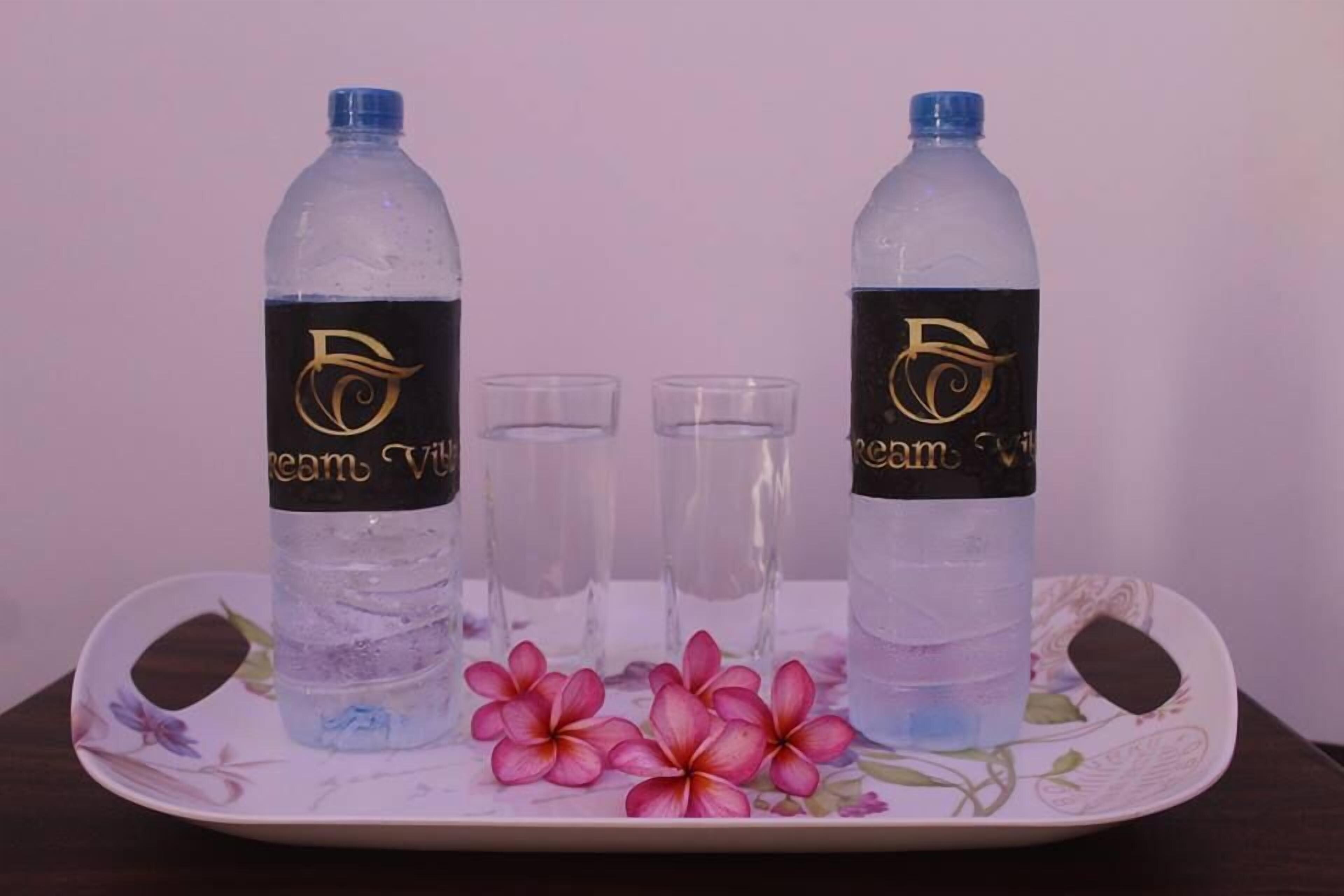 Deux bouteilles d’eau « Dream V », deux verres transparents et une assiette à motifs floraux sur une table.
