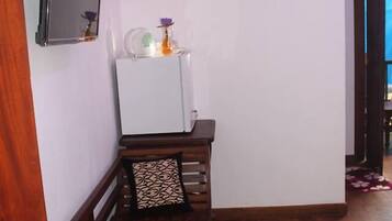 A compact room with a wooden bench, a white refrigerator, a flat-screen TV mounted on the wall, and a door leading to another area.