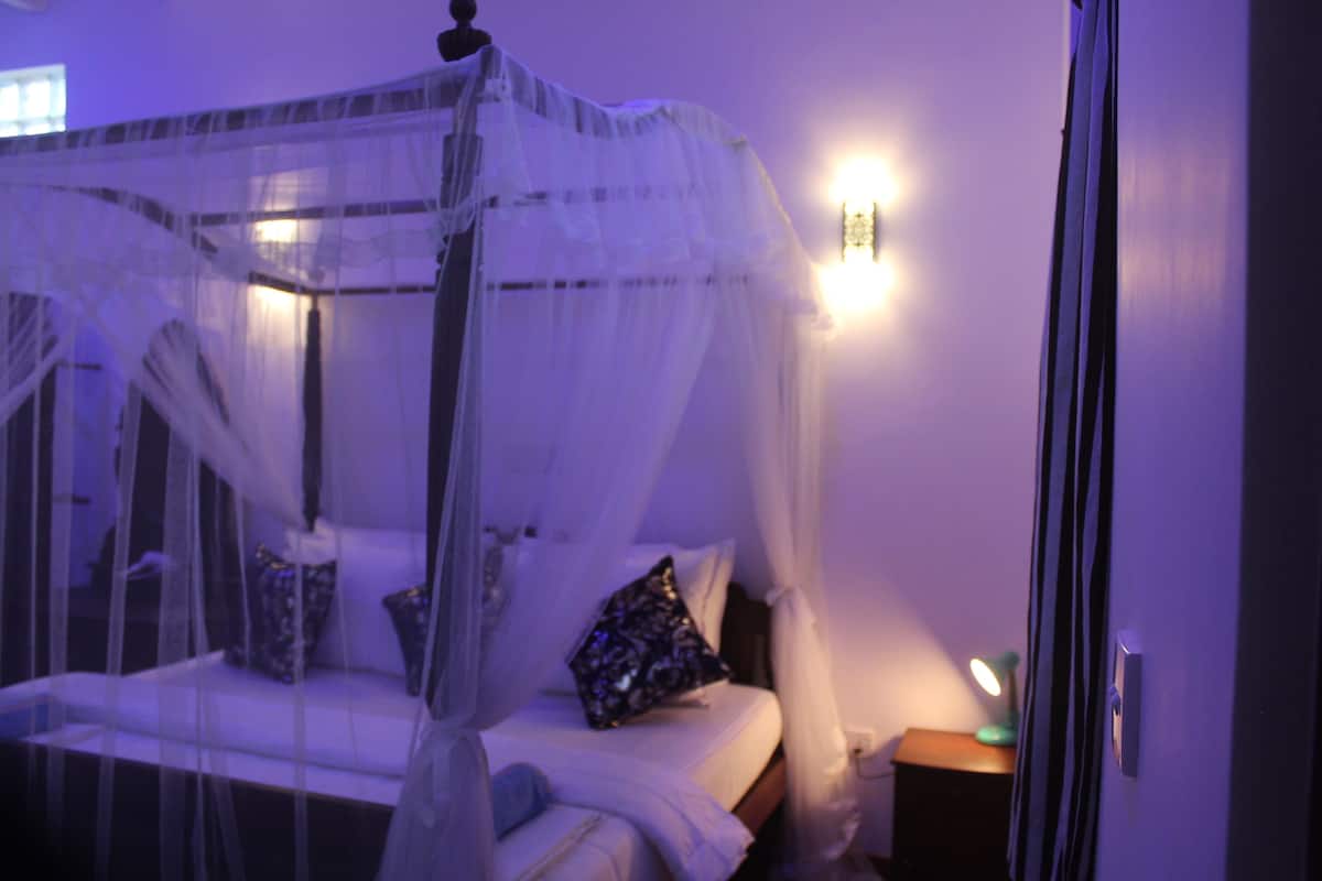 Un dormitorio con cama con dosel, mesitas de noche y una lámpara de pared.
