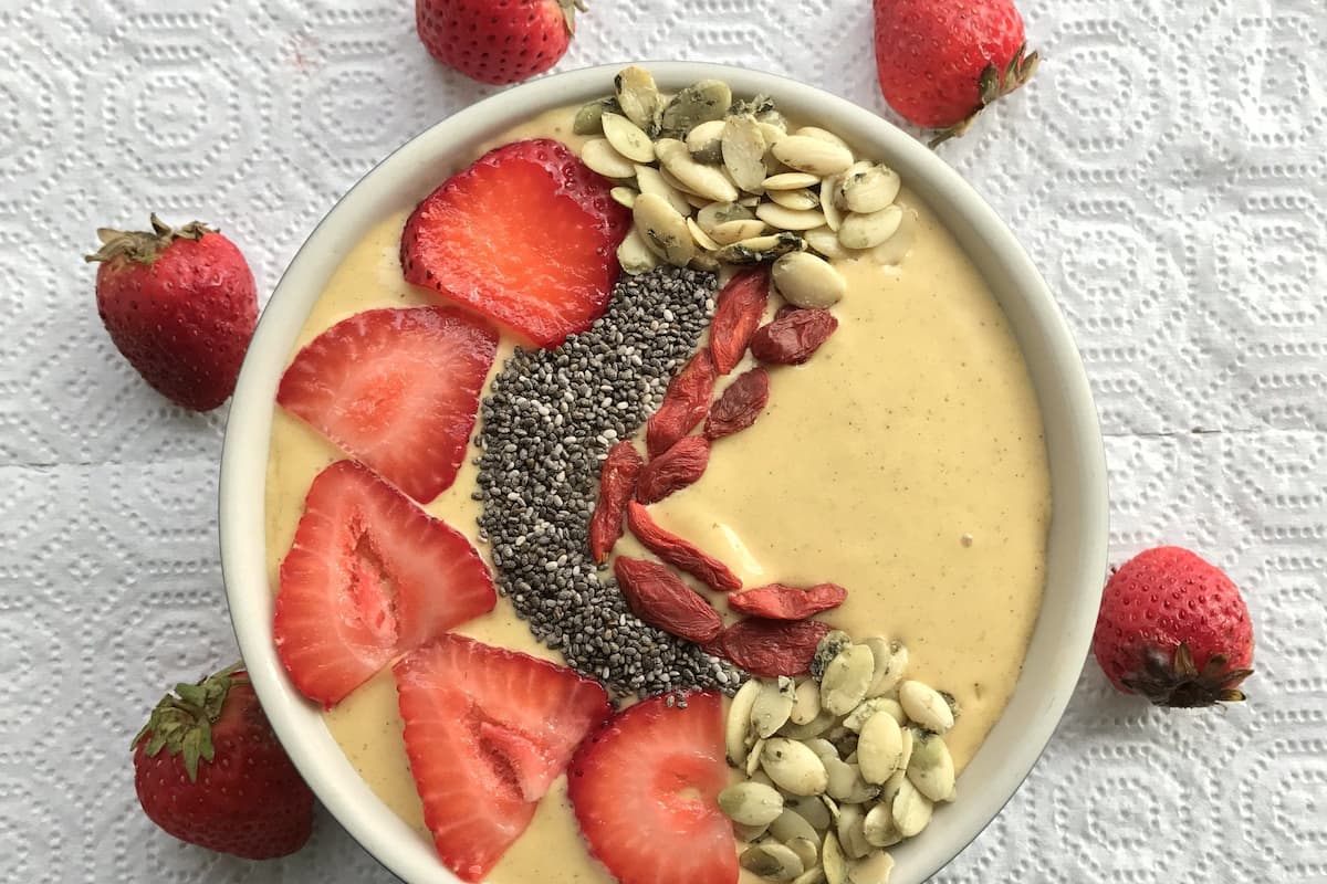 Un tazón de batido con fresas, semillas de chía y nueces sobre una superficie blanca texturizada.