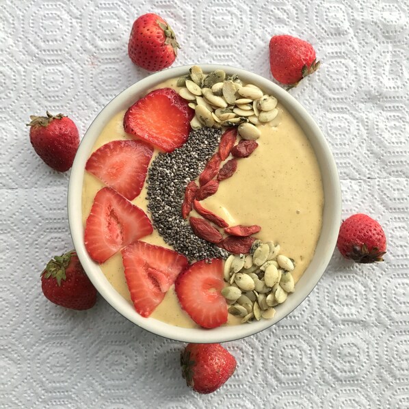 A bowl of smoothie with strawberries, chia seeds, and nuts on a white textured surface. - Dream Villa (Galle)