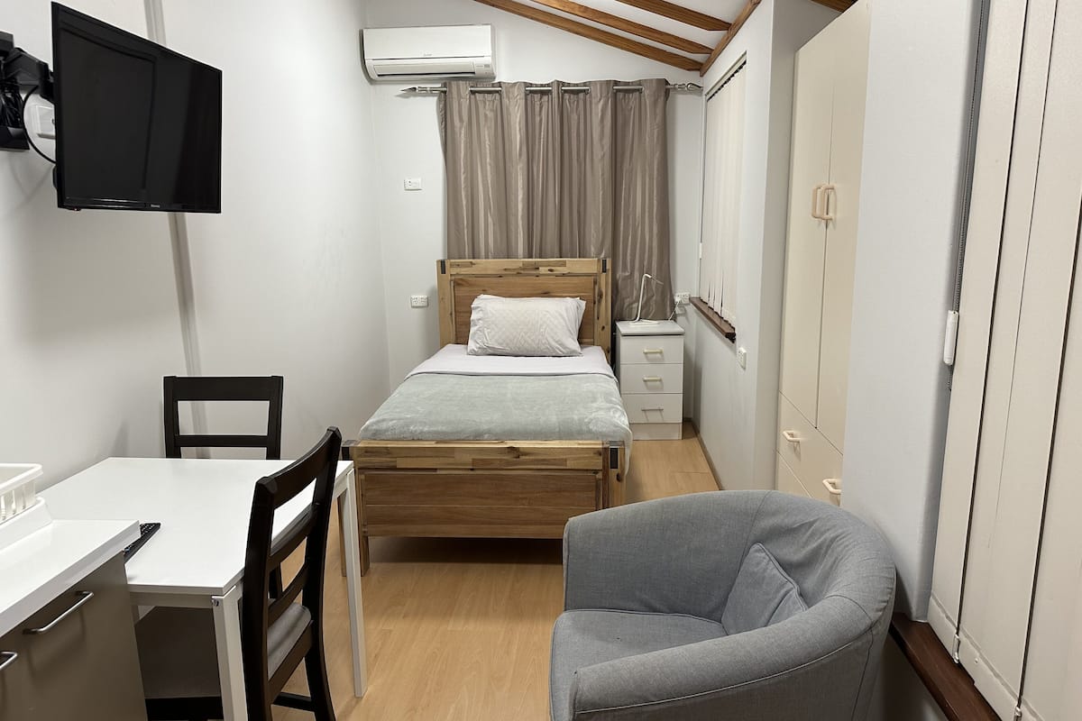 Une chambre de taille modeste, comprenant un lit, un bureau, une chaise, un téléviseur et un appareil de climatisation.
