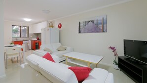 En moderne stue med sofa, sofabord, fjernsyn og et køkken i baggrunden.