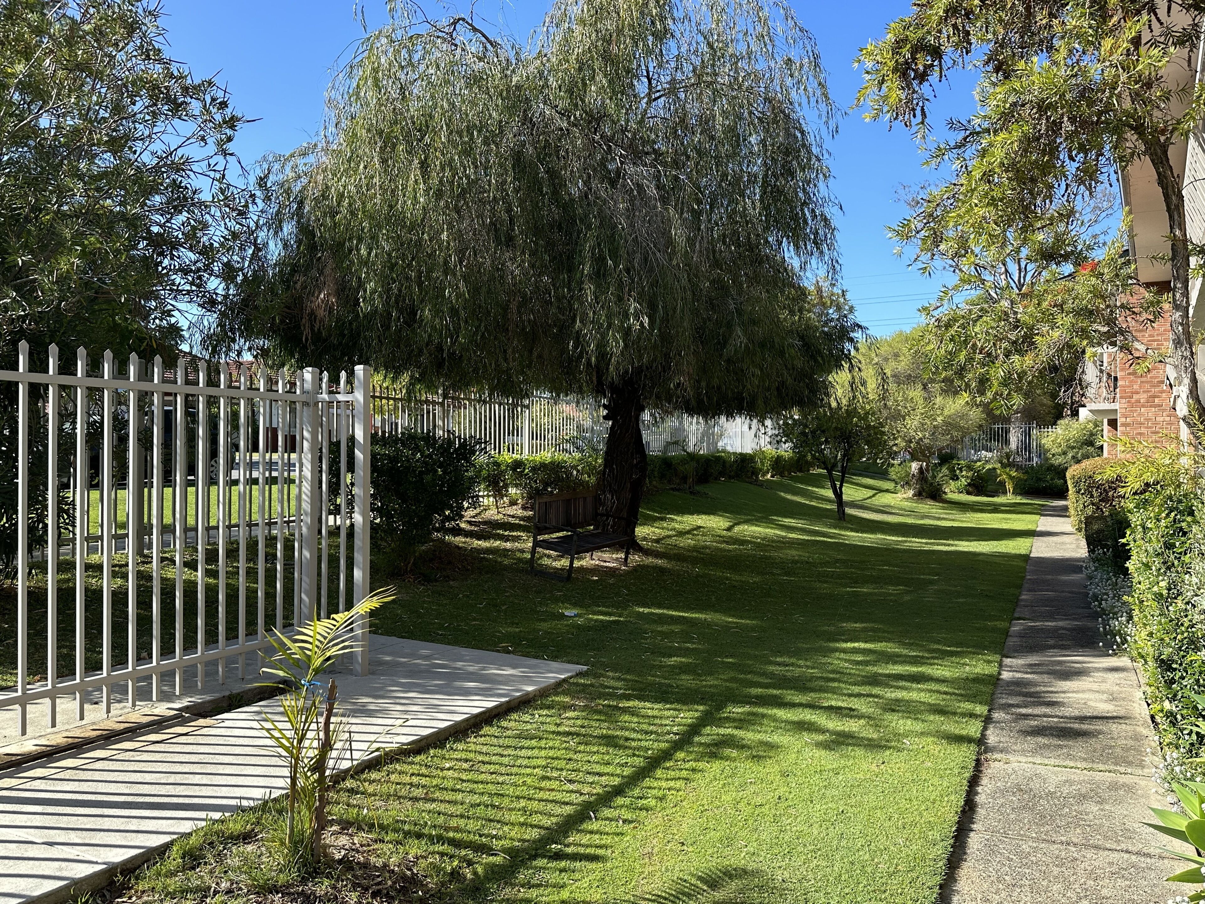 A well-maintained garden with a white fence, a paved walkway, and a bench.