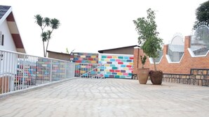 A courtyard with a colorful brick wall, a white metal fence, and two large planters. - Mama Rwanda Youth Hostel (Kigali)