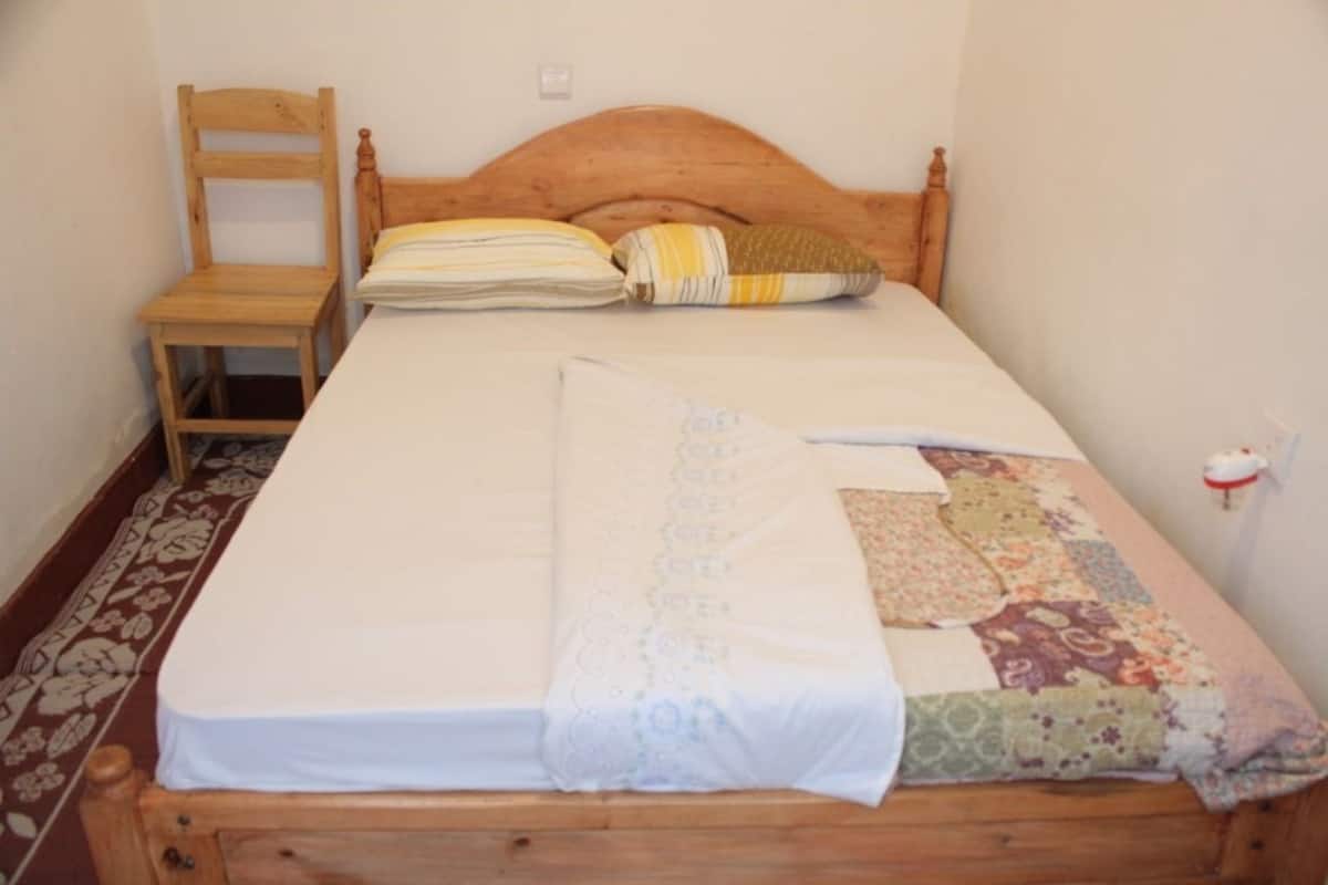 A single bed with a wooden headboard, a wooden chair, and a patterned blanket.