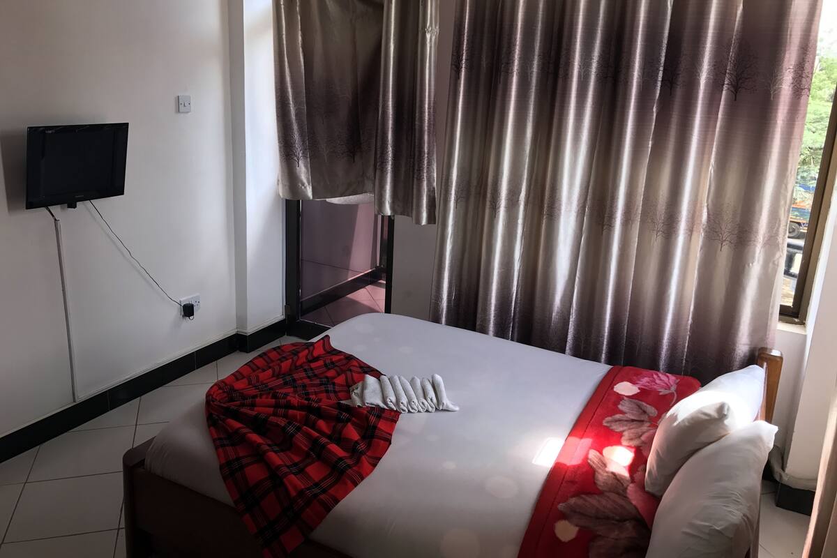 A hotel room with a bed, a TV mounted on the wall, and a window with curtains.