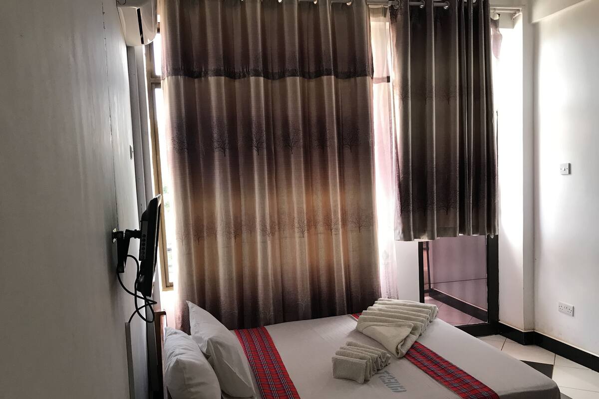 A hotel room with a bed, pillows, a blanket, and a window with curtains.