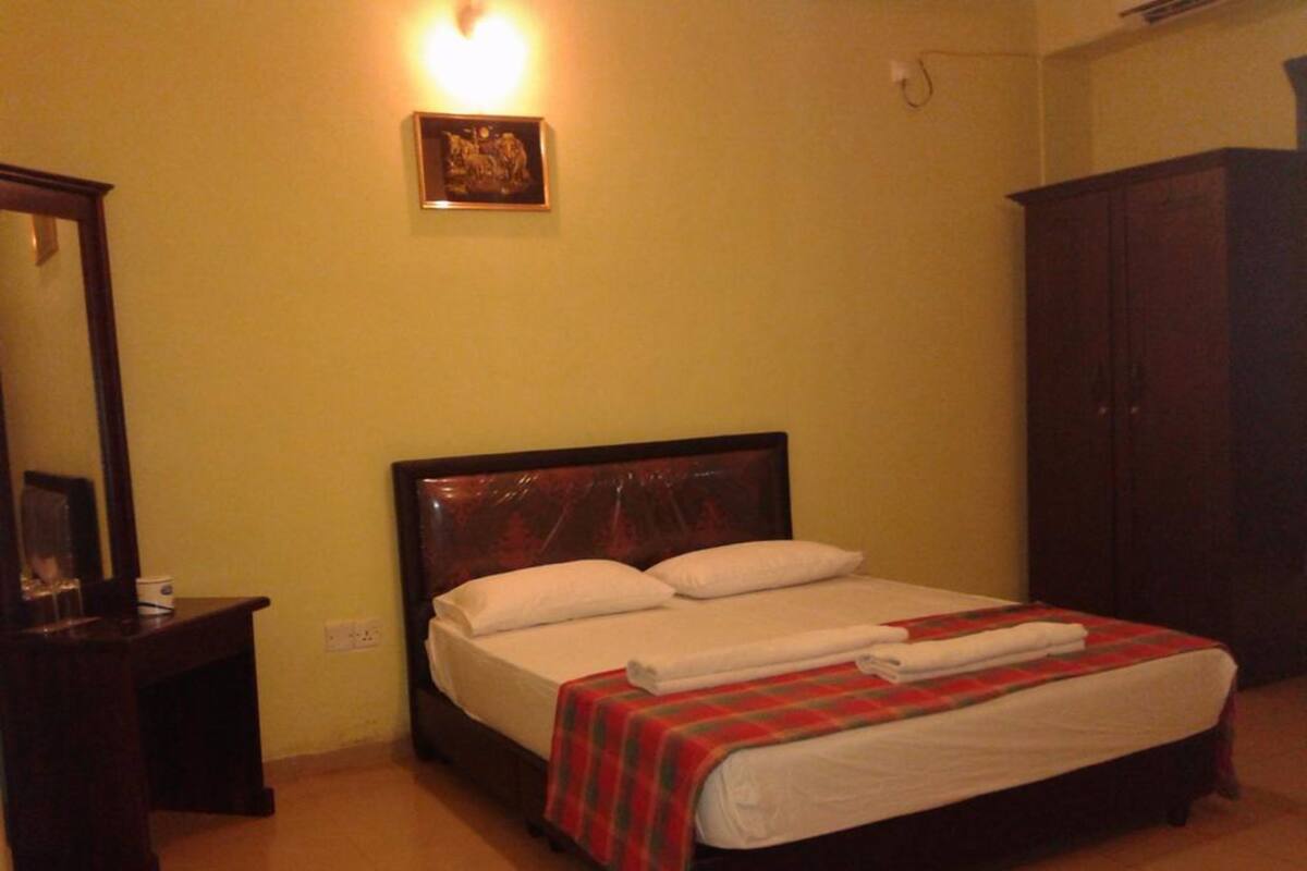 Una habitación de hotel con cama, mesita de noche, armario y una lámpara fijada a la pared.