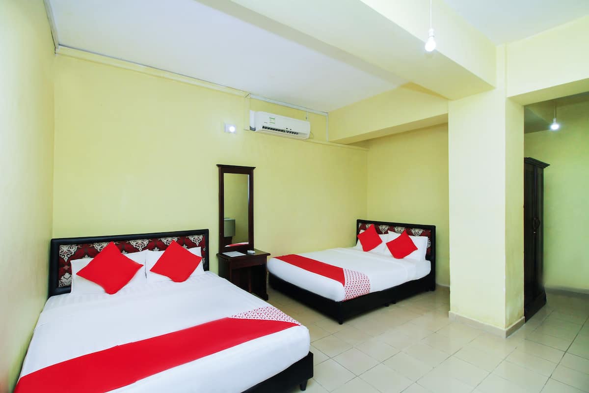 Habitación de hotel con dos camas, cada una con ropa de cama roja y blanca, un espejo, una mesita de noche y un equipo de aire acondicionado.