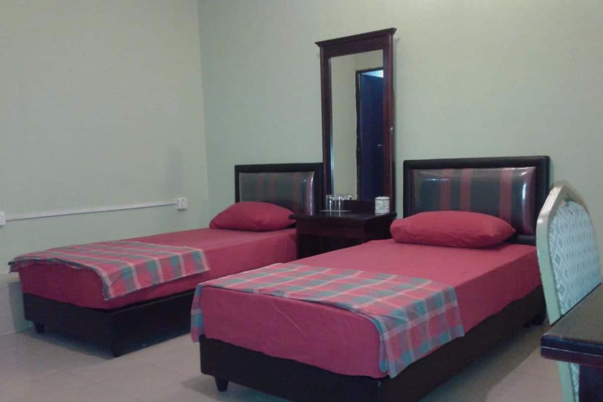 Una habitación con dos camas individuales, cada una con una colcha roja y almohadas a juego. Se ve un espejo grande sobre las camas y una mesita pequeña a la derecha.