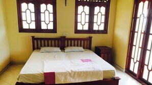 A bedroom with a wooden bed, two windows with decorative glass, a bedside table, and a small nightstand. - Eliyana Guest House (Thalaramba)