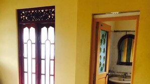 A bedroom with a bed, a window with a decorative grille, and a bathroom visible through an open door. - Eliyana Guest House (Thalaramba)