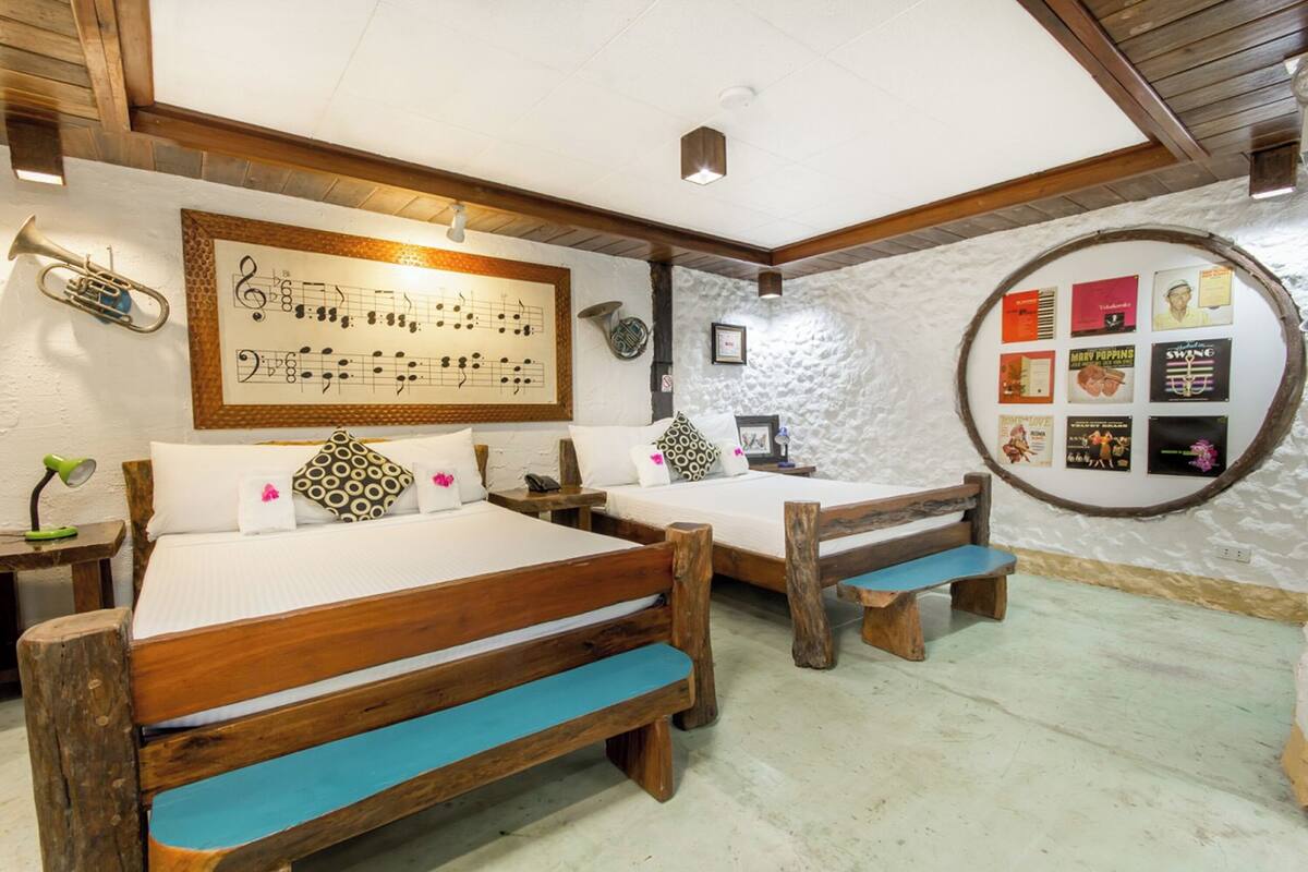 A rustic room with two wooden beds, a wall-mounted music sheet, and a circular display of framed items.