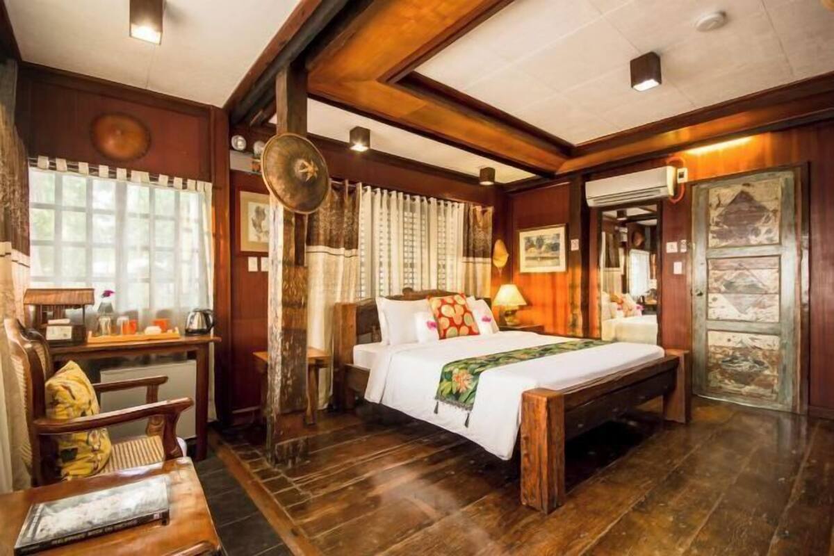 A traditional room with a bed, wooden furniture, a desk, and a large fan.